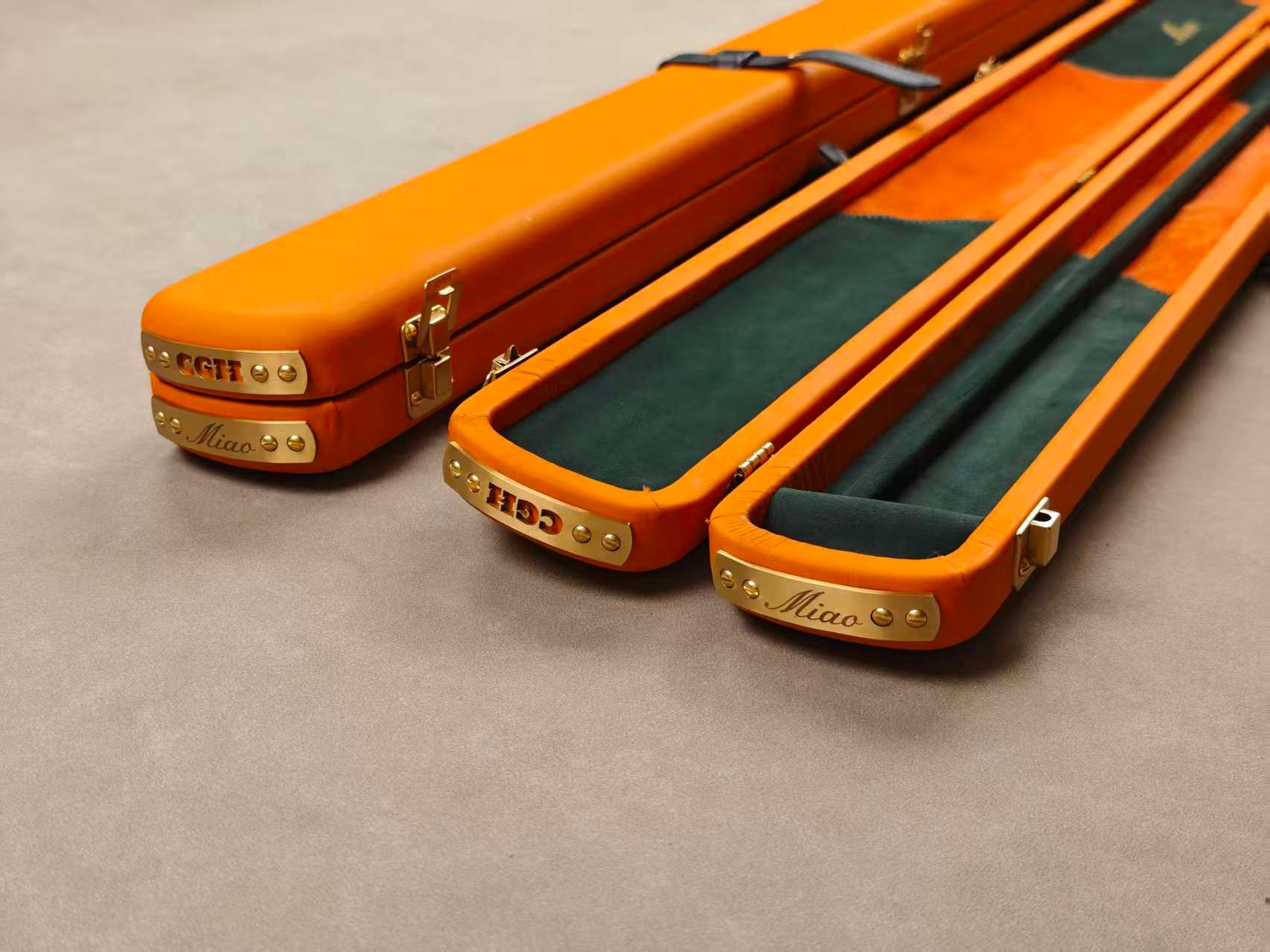 Orange leather cue cases with green interiors and personalised metal plates
